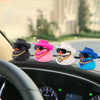 A collection of pink, white, and blue cowboy hat rubber duck car dashboard decorations on a car interior.