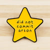 A yellow star enamel pin with black edging featuring the text did not commit arson.