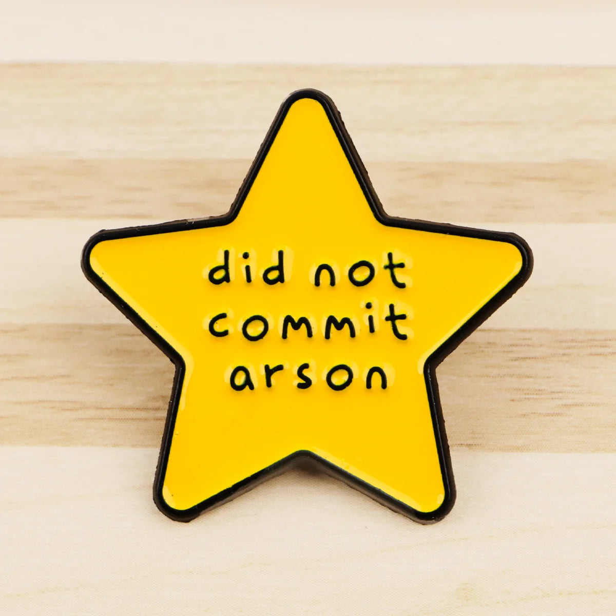 A yellow star enamel pin with black edging featuring the text did not commit arson.