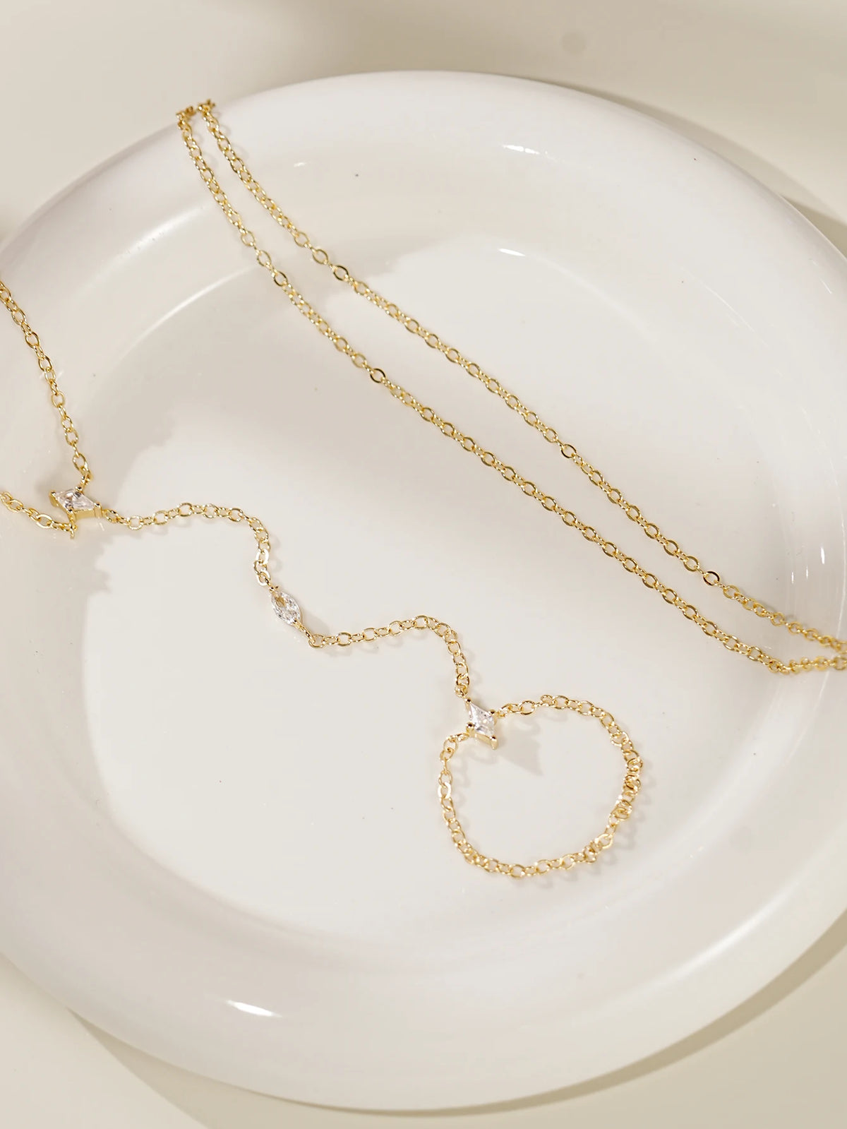 Gold ultra-thin layering chain necklaces with small diamond accents displayed on a white plate.