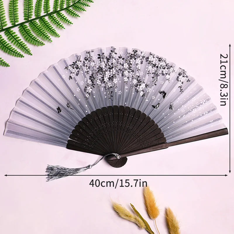 Elegant black and silver bamboo folding hand fan with a tassel displayed on a white background.