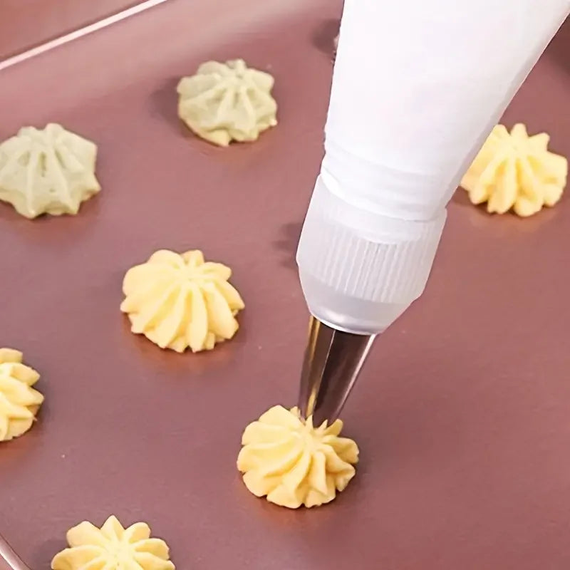 A white piping nozzle is decorating light yellow frosting shapes on a brown surface.