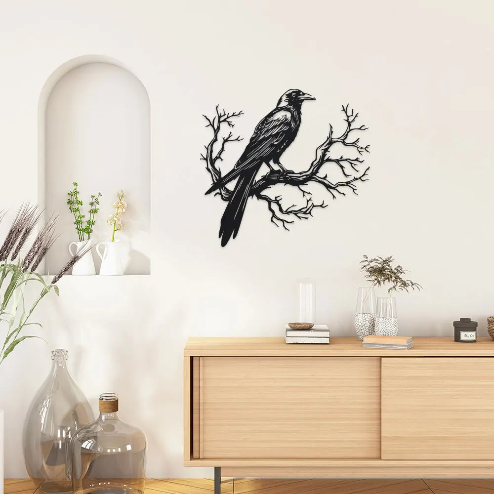 Black raven perched on a bare tree branch metal wall art displayed above a wooden cabinet.