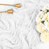 Gold-toned metal utensils resting on a white, flowing cheesecloth fabric with white and yellow flowers.