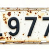 A vintage aluminum license plate tag with the year 1977 showing signs of wear and patina.