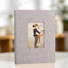 A square linen photo album with a front display window showing a couple embracing.