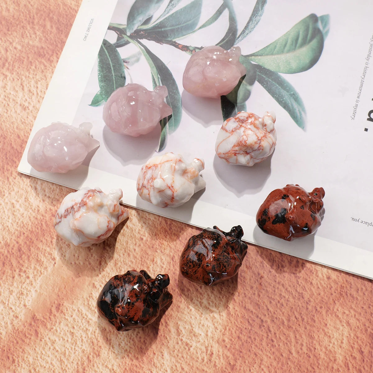 A collection of natural crystal heart carvings in pink, white, and dark brown tones displayed on a light background.
