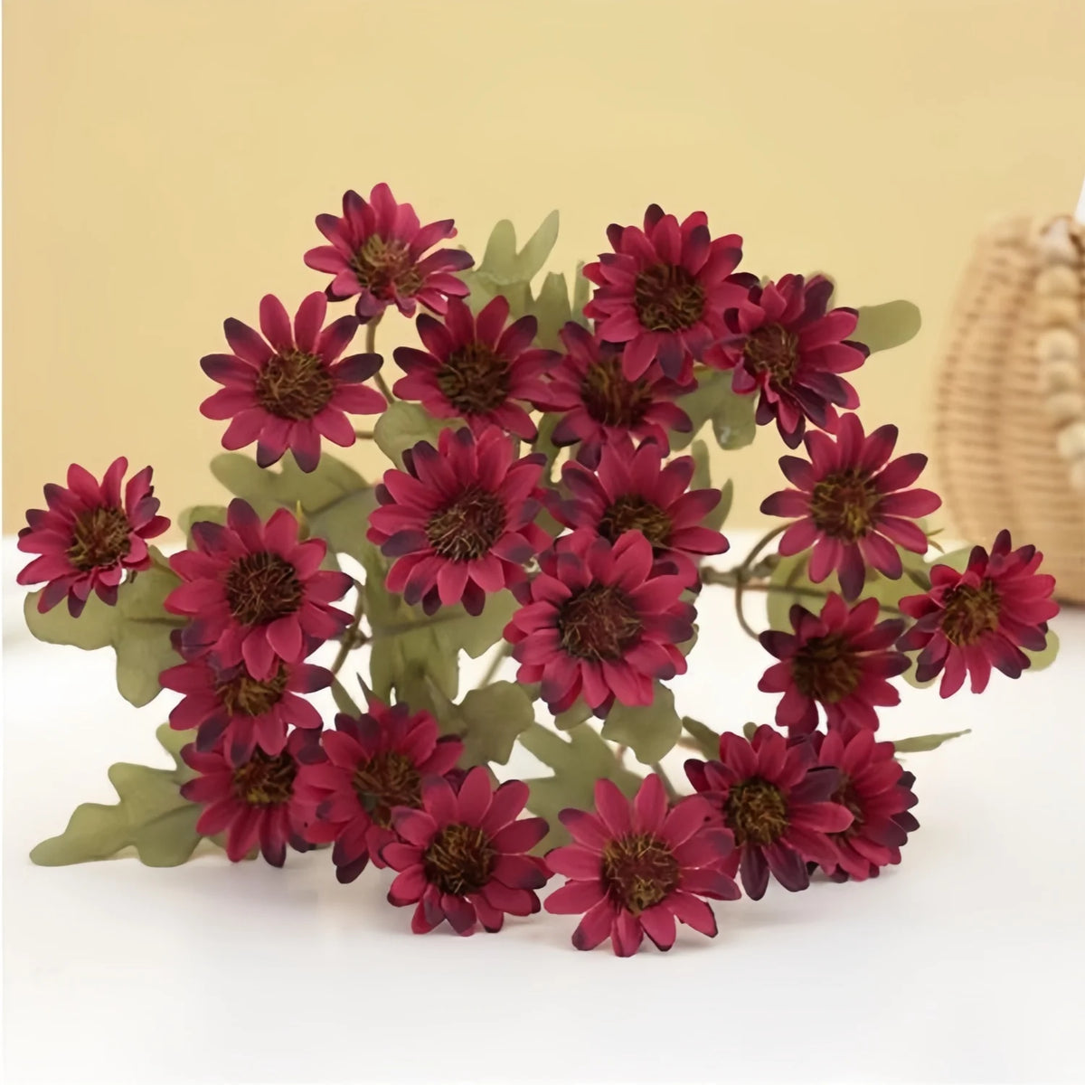 A cluster of three lifelike silk gerbera daisy artificial flowers in deep burgundy and green foliage.