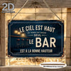A vintage metal tin sign with text that reads Le ciel est haut la terre est basse le bar est à la bonne hauteur, displayed on