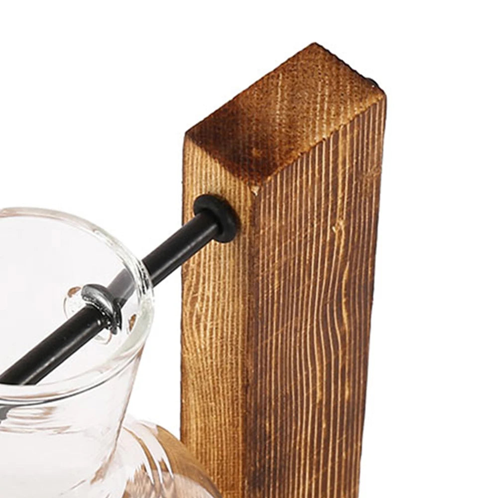 A glass hydroponic terrarium vase is shown resting on a vertical wooden stand.