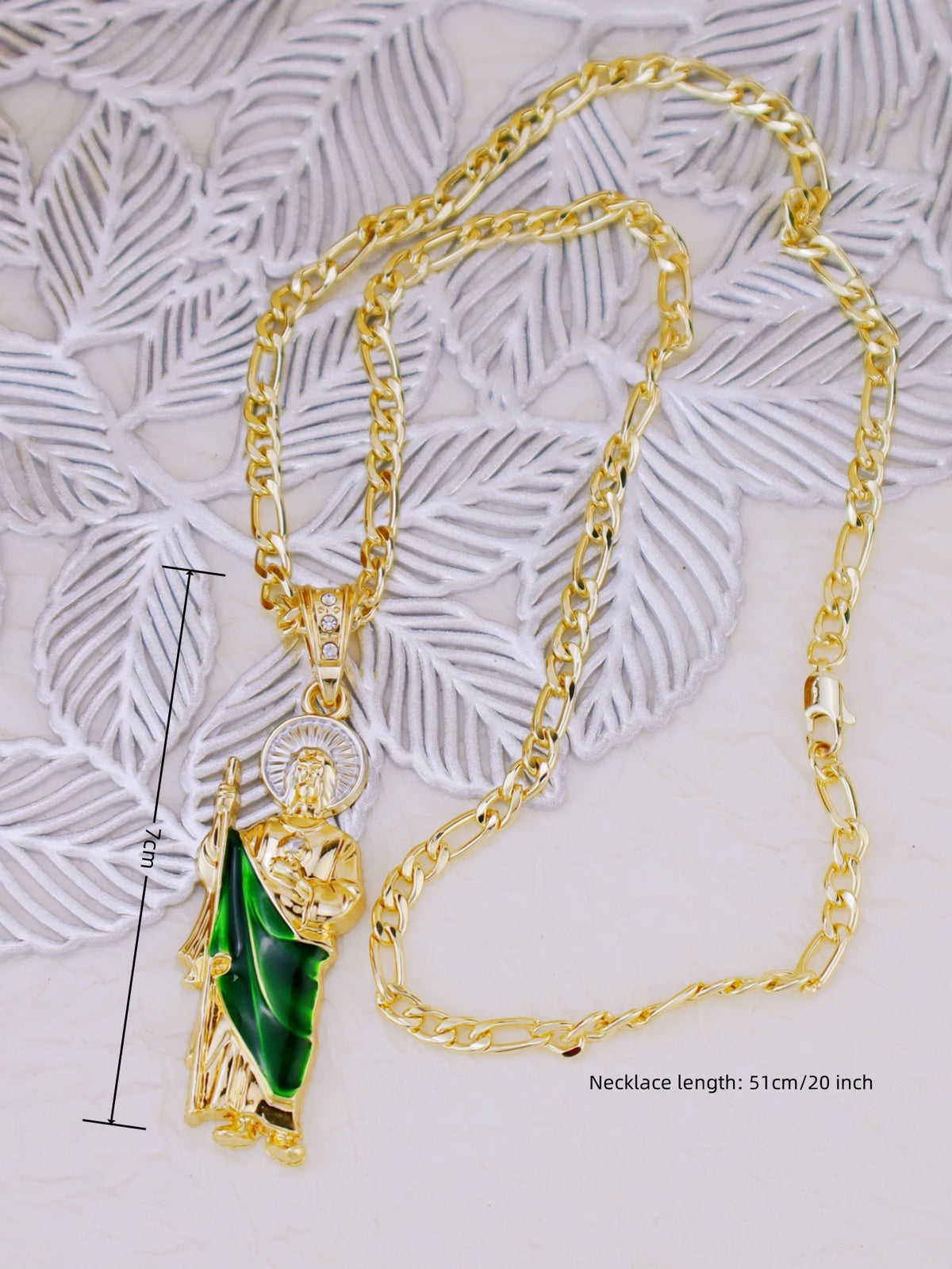 A gold-plated pendant necklace featuring a figure of Saint Jude, set against a white lace background.