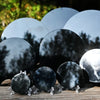 A collection of smooth, dark obsidian mirrors are displayed on a wooden surface.