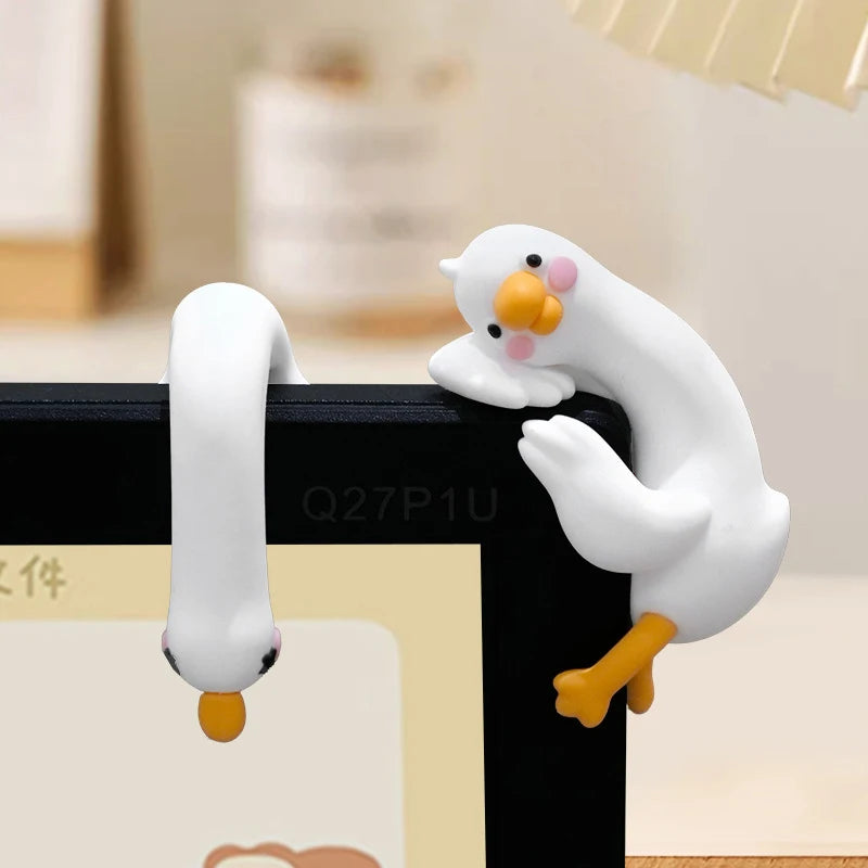 Figurine de canard en céramique ou résine blanche avec des pattes jaunes, posée sur une surface noire.
