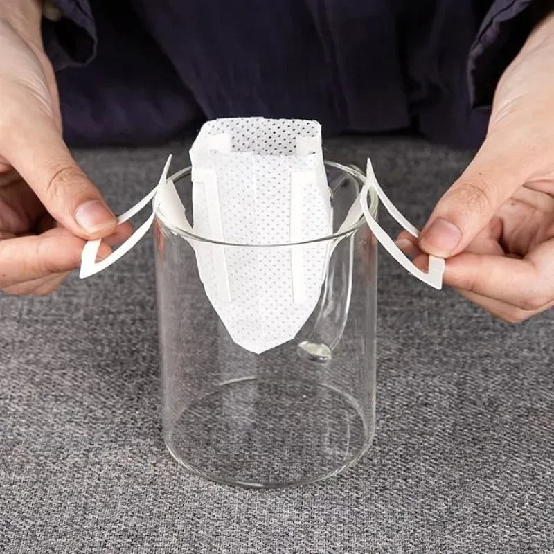 Hands holding white disposable coffee filter bags over a glass container for pour-over brewing