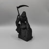 A black figurine of a female grim reaper with a hood and flowing robes holding a scythe.
