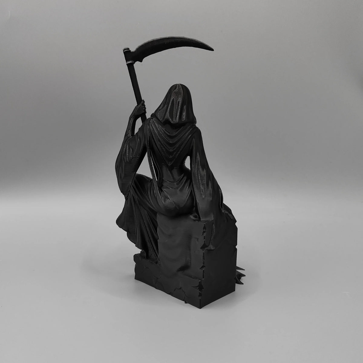 A black figurine of a female grim reaper with a hood and flowing robes holding a scythe.