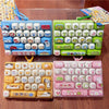 A collection of colorful cartoon animal keycap keychains and fidget toys arranged on a wooden surface.