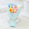 A bouquet of handmade crochet flowers in pastel blue, yellow, and purple arranged in a folded paper presentation.