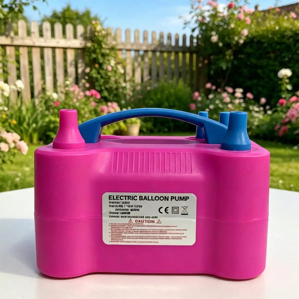 A pink electric balloon pump device resting on a white surface outdoors.