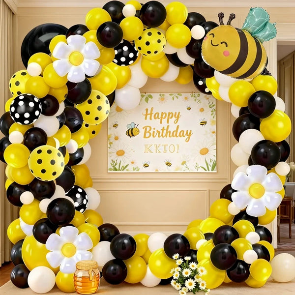 A yellow, black, and white balloon arch set decorated with bees and daisies for a birthday celebration.