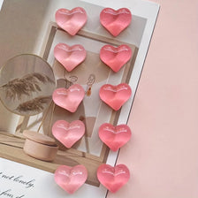 A set of ten heart-shaped pink resin magnets arranged on a light wooden surface.