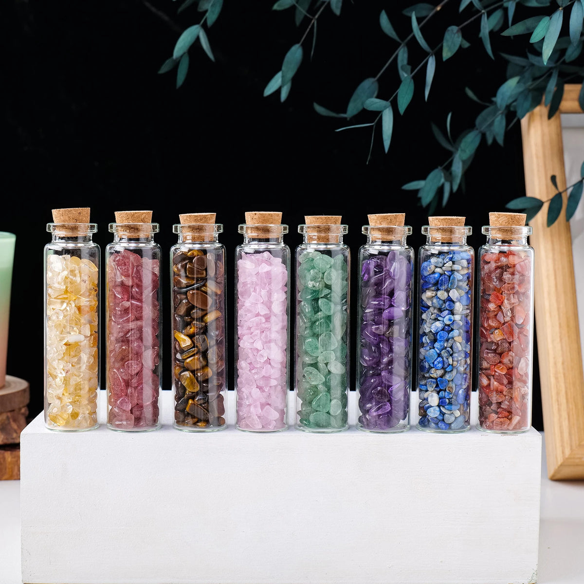 A row of natural crystal healing drifting bottles filled with various colored crystals displayed on a white surface.