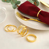 Ein Set eleganter goldener Metallserviettenringe und ein tiefrotes Seidenserviett auf einem weißen Teller.