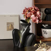 A black ceramic figural vase shaped like an artistic human form holding a bouquet of pink and peach hydrangeas.