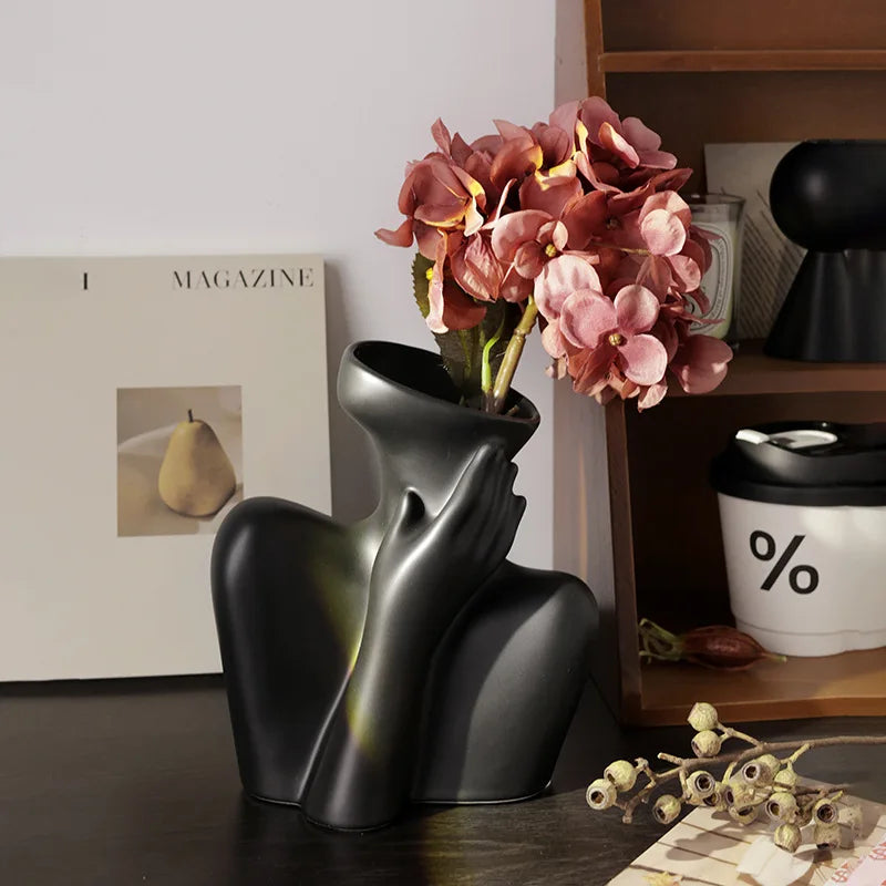 A black ceramic figural vase shaped like an artistic human form holding a bouquet of pink and peach hydrangeas.