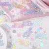 Holographic disco confetti in various pastel colors scattered on a pink satin fabric.