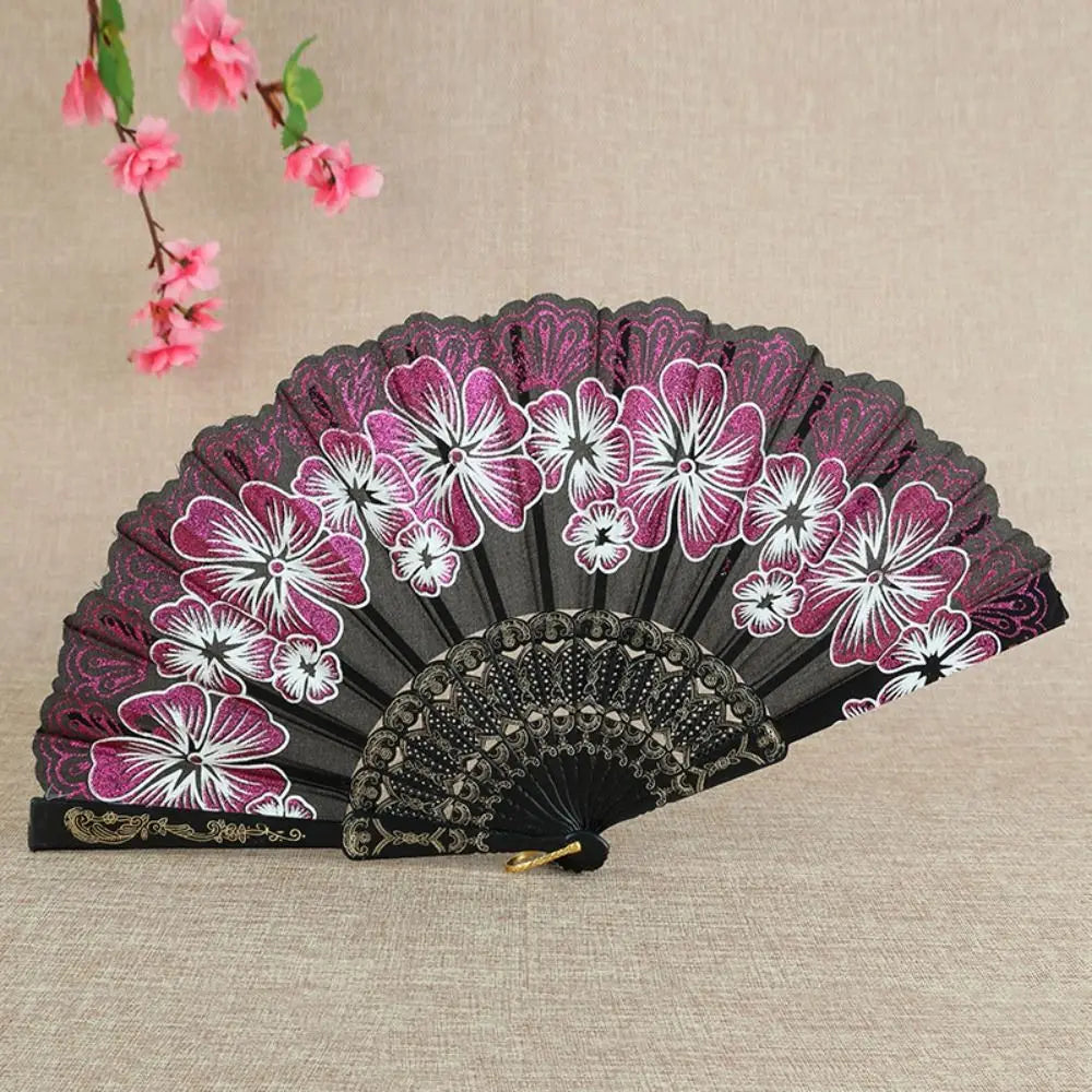 A folding fan with a black background featuring pink and white floral patterns.