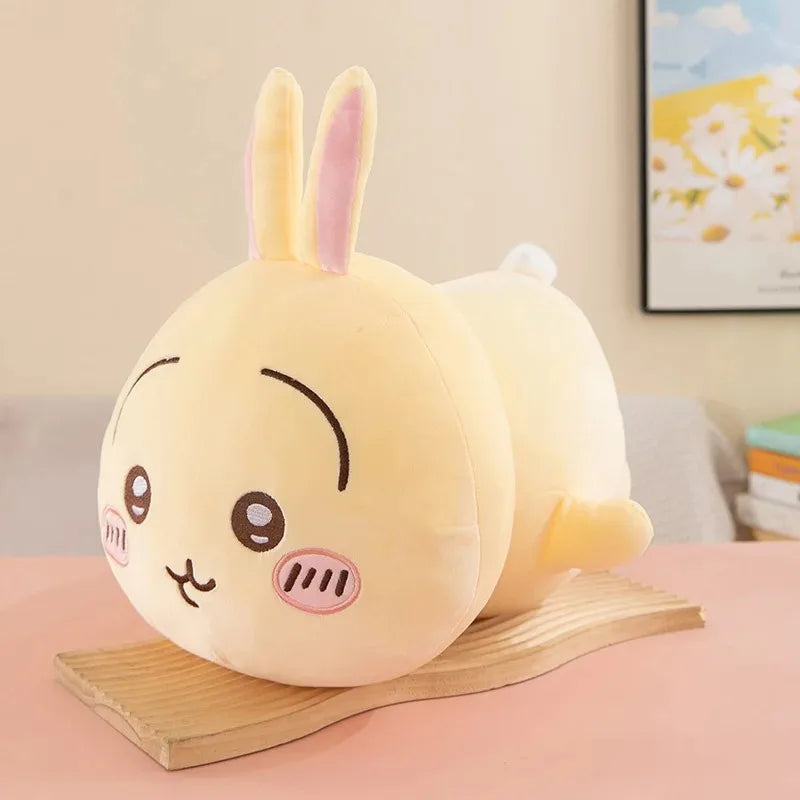 A soft yellow Chiikawa Hachiware plush pillow with pink ears resting on a wooden surface.