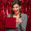 A woman smiling while holding a red tablet in front of a silver metallic foil fringe curtain backdrop.