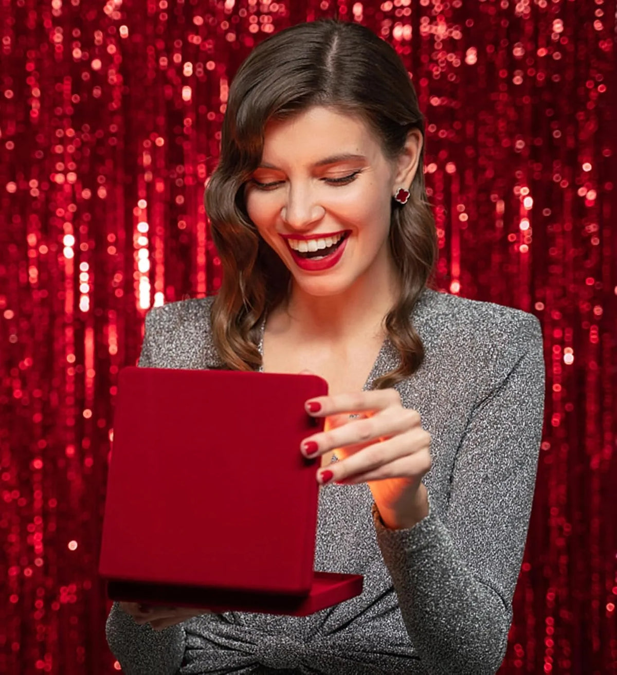 A woman smiling while holding a red tablet in front of a silver metallic foil fringe curtain backdrop.