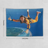 A tapestry featuring a man in an orange shirt jumping with his arms outstretched against a blue sky and view of the Earth.