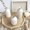 Three white ceramic vases of varying sizes displayed on a natural wood tray atop a crocheted textile.