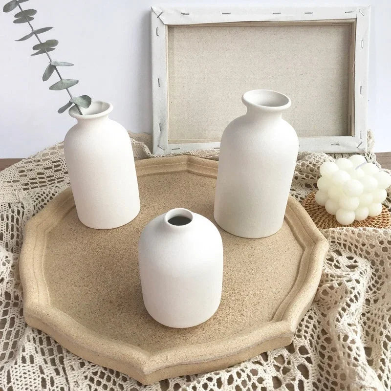 Three white ceramic vases of varying sizes displayed on a natural wood tray atop a crocheted textile.