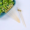 Gold accent bamboo cocktail skewers with spherical balls arranged next to sliced kiwi fruit