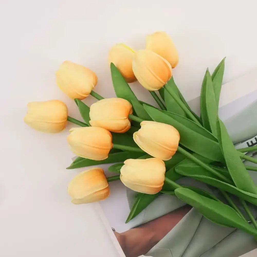 A bouquet of yellow artificial tulips with green leaves arranged on a white surface.