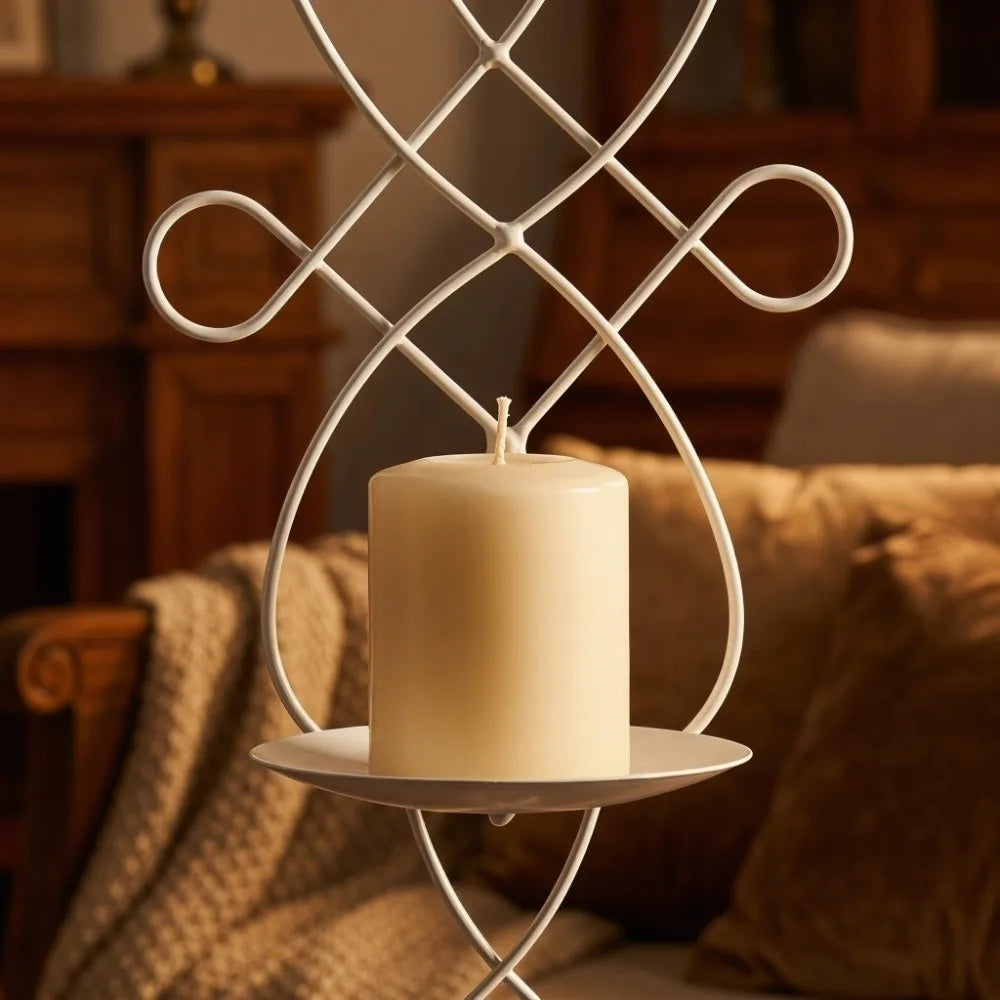 A white decorative iron wall candle sconce holding a cream-colored pillar candle on a small plate.