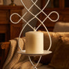 A white decorative iron wall candle sconce holding a cream-colored pillar candle on a bedside table.