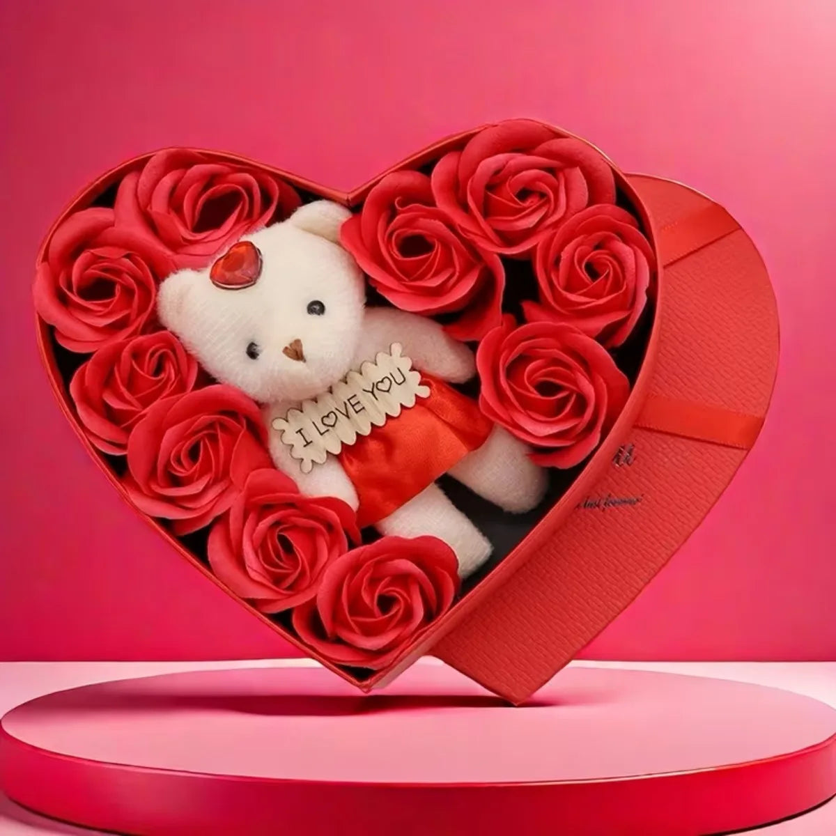 A red heart-shaped gift box filled with artificial red roses and a white plush bear wearing a red outfit.