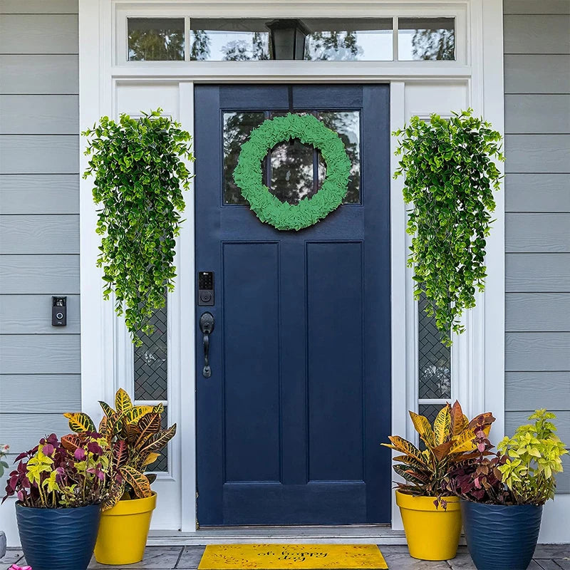 A dark blue front door decorated with a green wreath and flanked by artificial eucalyptus plants in yellow pots.