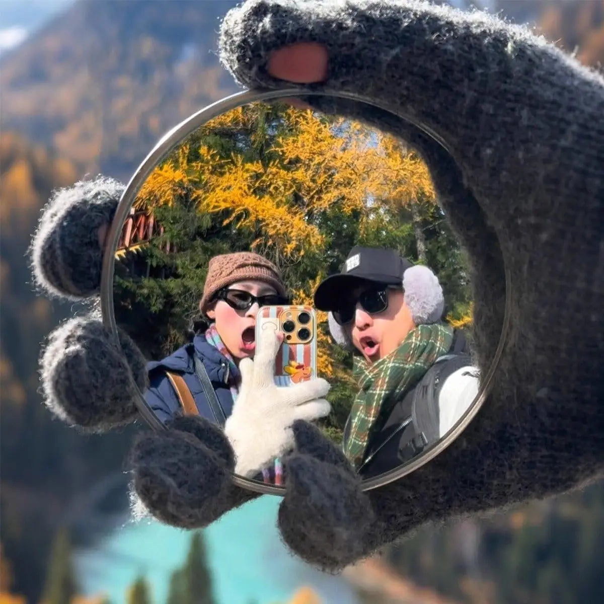 Eine Hand hält einen konvexen Spiegel, der ein Selfie einer Person inmitten von Herbstlaub im Freien macht.
