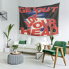 A large red and black tapestry with white text that reads Get Out of Your Head hanging on a white wall.