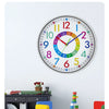 A colorful silent wall clock with numbered faces is displayed on a white wall above a wooden cabinet and small furniture.