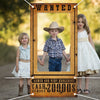 A wooden photo booth backdrop framed in gold featuring a cowboy hat and two young girls standing in front of a blurred outdoo