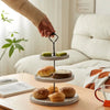 A hand is placing a cupcake on a wooden 3-tier stand with detachable layers.