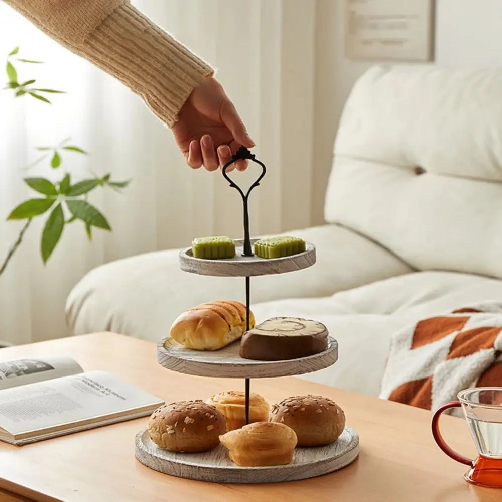 A hand is placing a cupcake on a wooden 3-tier stand with detachable layers.