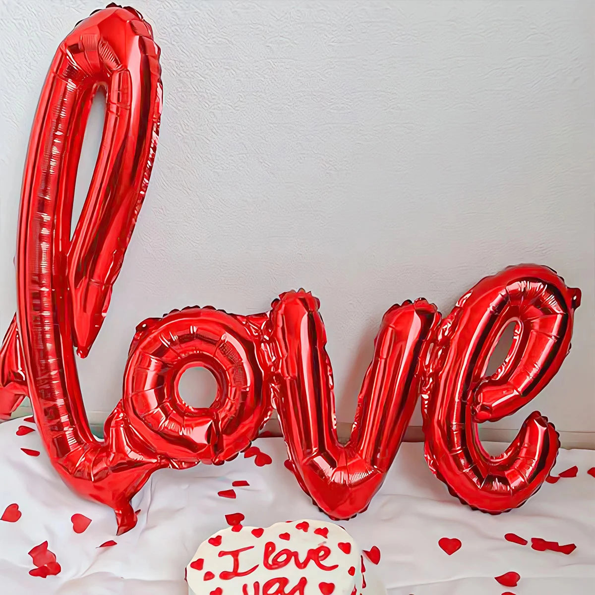 Rote Folienherzballons, die LOVE buchstabieren, mit einem kleinen Kuchen im Vordergrund